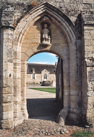 La porte piétonne de la porterie du XIIIe siècle de Longues est surmontée d’une statue de Saint Jacques. La porte avec un arc surbaissé s’inscrit dans une arcature en ogive. On aperçoit dans le fond le logis abbatial édifié au XIIe siècle (pour le rez-de-chaussée conservé) modifié au XIVe siècle puis, ici, au XVIIIe siècle. (Photo Georges Bernage © Patrimoine Normand)