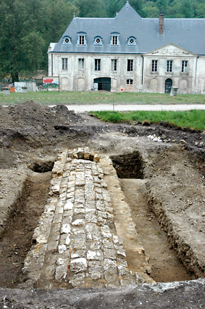 Le « canal des moines » qui amène les eaux de la rivière au monastère ; sa voûte surbaissée est bloquée par les piédroits de la canalisation. Il se poursuit, au-delà de la fouille, sous la pelouse et a été suivi jusqu’au droit du mur visible en fond. (Photo Erik Follain © Patrimoine Normand)