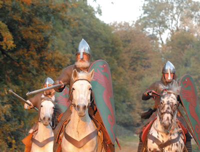 Reconstitution d’une charge de cavalerie au XIe siècle, Hastings 2006. Les cavaliers normands écrasent les lignes adverses sous la violence du choc, grâce à la lance. Mais le harnachement du cheval est aussi essentiel dans le succès. Ce sont les mors qui vont le stimuler et le guider, ainsi que les éperons. Mais c’est aussi une selle enveloppante dans laquelle le cavalier se trouve emboîté pour ne pas être éjecté de son cheval en moment du choc. Cette selle est retenue par la bricole qui passe devant le poitrail du cheval et qu’on voit ici. Par ailleurs, l’introduction de l’étrier, dès la période caro­lingienne, permet au cavalier d’être mieux tenu sur son cheval ; c’est un important progrès. (© Histoire Vivante/F. Coune)