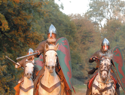 Reconstitution d’une charge de cavalerie au XIe siècle, Hastings 2006. Les cavaliers normands écrasent les lignes adverses sous la violence du choc, grâce à la lance. Mais le harnachement du cheval est aussi essentiel dans le succès. Ce sont les mors qui vont le stimuler et le guider, ainsi que les éperons. Mais c’est aussi une selle enveloppante dans laquelle le cavalier se trouve emboîté pour ne pas être éjecté de son cheval en moment du choc. Cette selle est retenue par la bricole qui passe devant le poitrail du cheval et qu’on voit ici. Par ailleurs, l’introduction de l’étrier, dès la période caro­lingienne, permet au cavalier d’être mieux tenu sur son cheval ; c’est un important progrès. (© Histoire Vivante/F. Coune)
