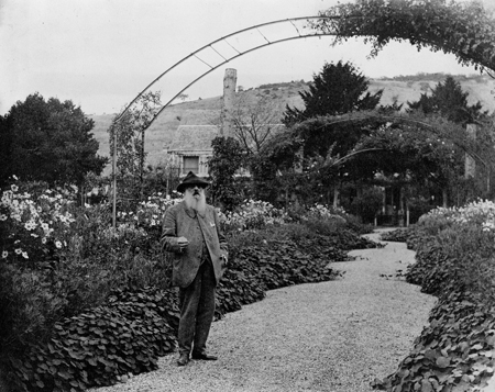 Claude Monet dans son allée centrale, sous les immenses arceaux métalliques qui ont remplacé les conifères. Y grimpaient surtout deux variétés : Crimson Rambler et La Belle Vichyssoise. Les modestes églantiers avaient aussi sa faveur. (© Coll. Fondation Claude Monet)