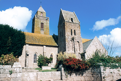 L’église paroissiale de Gatteville avec ses deux clochers. Au premier plan, le clocher avec son toit en bâtière caractéristique du Cotentin, seul vestige de l’église romane primitive. Au second plan le clocher bâti au XVIIIe siècle a nettement moins de caractère. Le cimetière, désaffecté, comprend quelques vieilles pierres tombales du XIXe siècle ainsi qu’une croix hosannière en granit. (Photo François de Lannoy © Patrimoine Normand)