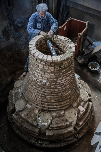 Au commencement de la fabrication du moule d'une cloche l'on fabrique le noyau, en briques réfractaires et en argile. Le noyau correspondra à l'espace vide à l'intérieur de la cloche finie. Il supportera le moule jusqu'à la coulée. Sur cette image Daniel, ouvrier de la fonderie Cornille-Havard.à la réalisation du noyau.(© Vincent M.)