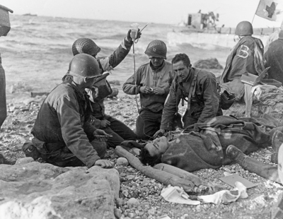 Transfusion de plasma pour des soldats blessés sur Omaha Beach. Tout comme ces hommes du secteur Fox Green, non loin des secteurs Charlie et Dog Green du 5th Ranger Battalion, on pratique des transfusions d’urgence pour sauver un maximum de vies. Cette photographie a été prise le 12 juin. (© Normandy Invasion, June 1944, SC 192575, National Archives)