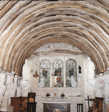 Chevet de la chapelle priorale. On aperçoit, de part et d’autre, les arcatures romanes, ainsi que deux colonnes, à gauche et à droite de ce chevet flanqué de statues du XIXe siècle de Saint Arnoul(t) et Saint Clair. La charpente était autrefois recouverte de lattes et de plâtre (© Amis du Prieuré de Saint Arnoul sur Touque)