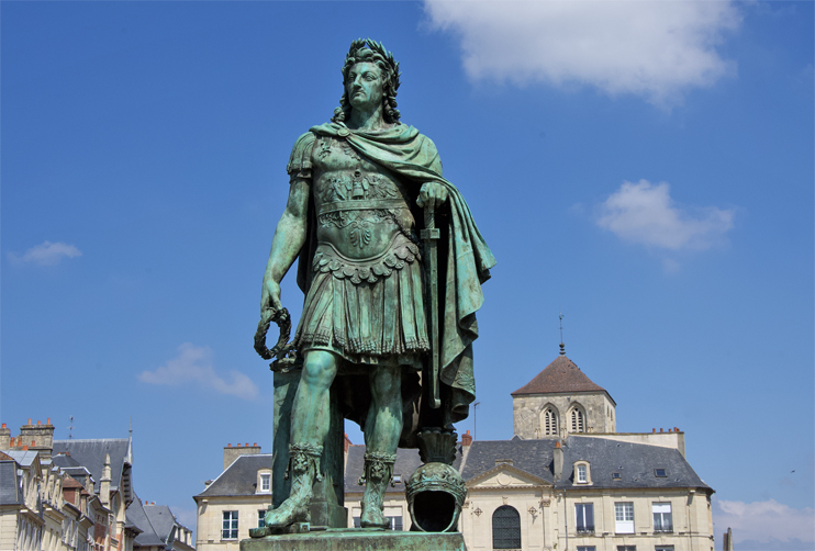 Louis XIV en empereur romain semble avoir toujours dominé la place Saint-Sauveur de Caen. En réalité, cette statue se trouvait depuis le 24 avril 1828 place Royale, devenue en 1883 place de la République ; cette année-là, on enlève l’œuvre pour la remplacer par… un kiosque à mu­sique ! Une première statue du Roi-Soleil sur cette même place avait été décidée en 1684 ; cette sculpture en pierre signée du Caennais Jean Postel est renversée et brisée pendant la Terreur, de sorte que le conseil municipal vote par délibération du 21 décembre 1819 le remplacement (cette fois-ci en bronze) de l’effigie de Louis-le-Grand, qui avait visité Caen le 5 septembre 1685, « cette ville connue pour son dévouement à ses Rois ». On confie la tâche au Parisien Louis-Messidor-Lebon Petitot, dit Louis Petitot, ancien pensionnaire du roi à l’académie de France, auteur de nombreuses œuvres académiques ou allégoriques, dont trois statues de Louis XIV. Sa composition générale, nous apprend le procès-verbal d’inauguration, a été déterminée d’après le choix fait entre divers projets de l’artiste par une commission de l’Institut, à laquelle le corps municipal en avait référé. Suivant l’intention qui a présidé à cette composition, la statue représente le monarque au moment où, rentré triomphant en France, il s’occupe du bonheur et de la gloire intérieure de son royaume par les encouragements qu’il donne aux sciences, aux arts et au commerce. En septembre 1827, pendant les travaux, la dauphine Marie-Charlotte passe à Caen où elle scelle « solennellement de sa main le bloc de marbre qui couronne le piédestal ». (Photo Rodolphe Corbin © Patrimoine Normand)